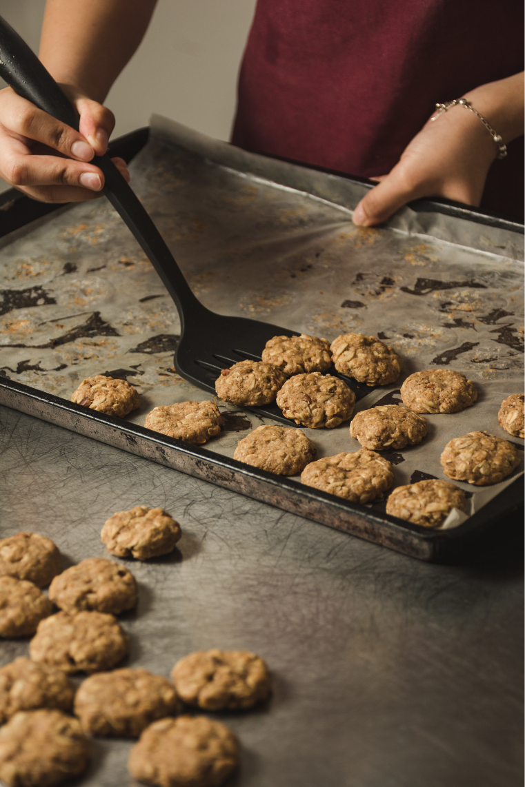 Preparando galletas se observan dos manos de una persona levantado galletas de una bandeja con una espatula